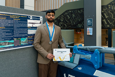 student standing proudly with prize at the innovations engineering showcase. They are stood in front of their final year project.