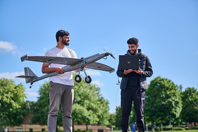 2 students stood at runway. One holding a UAV the other holding a laptop.
