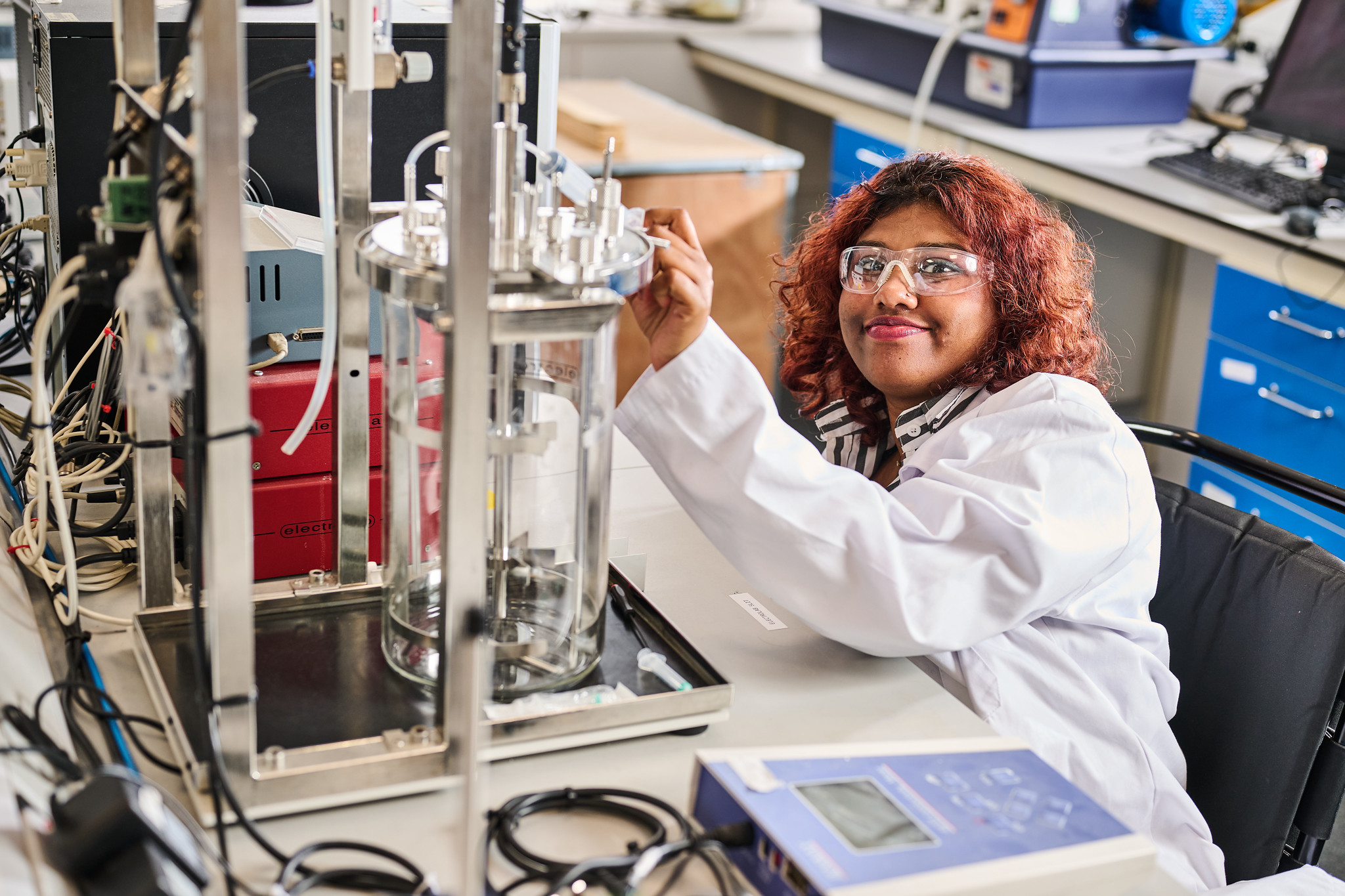 Chemical engineering student in white lab coat and safety goggles working in the chemical engineering lab at the city campus.
