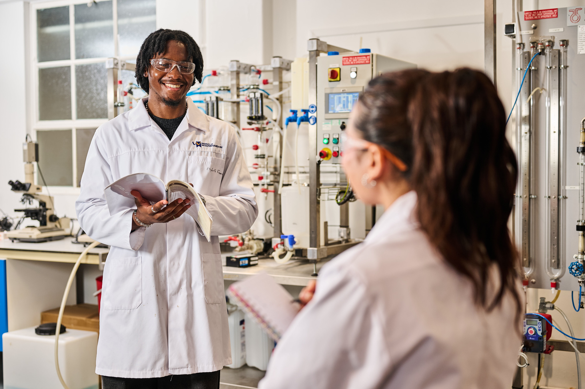 2 Chemical engineering students in white lab coats and safety goggles working in the chemical engineering lab at the city campus.