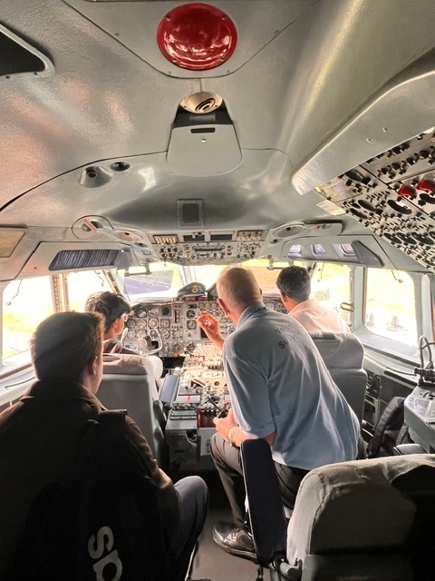 3 aerospace students are sat in the cockpit of an aircraft using the instruments as instructed by the instructer.