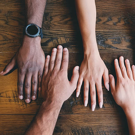 Four hands of different skin tones on a wooden surface