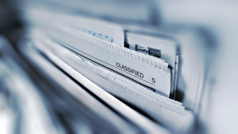 A pile of newspapers, with the word 'classified' visible at the top of one of the pages
