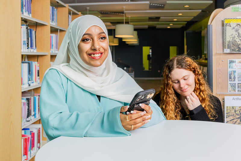 Student in library holding a phone