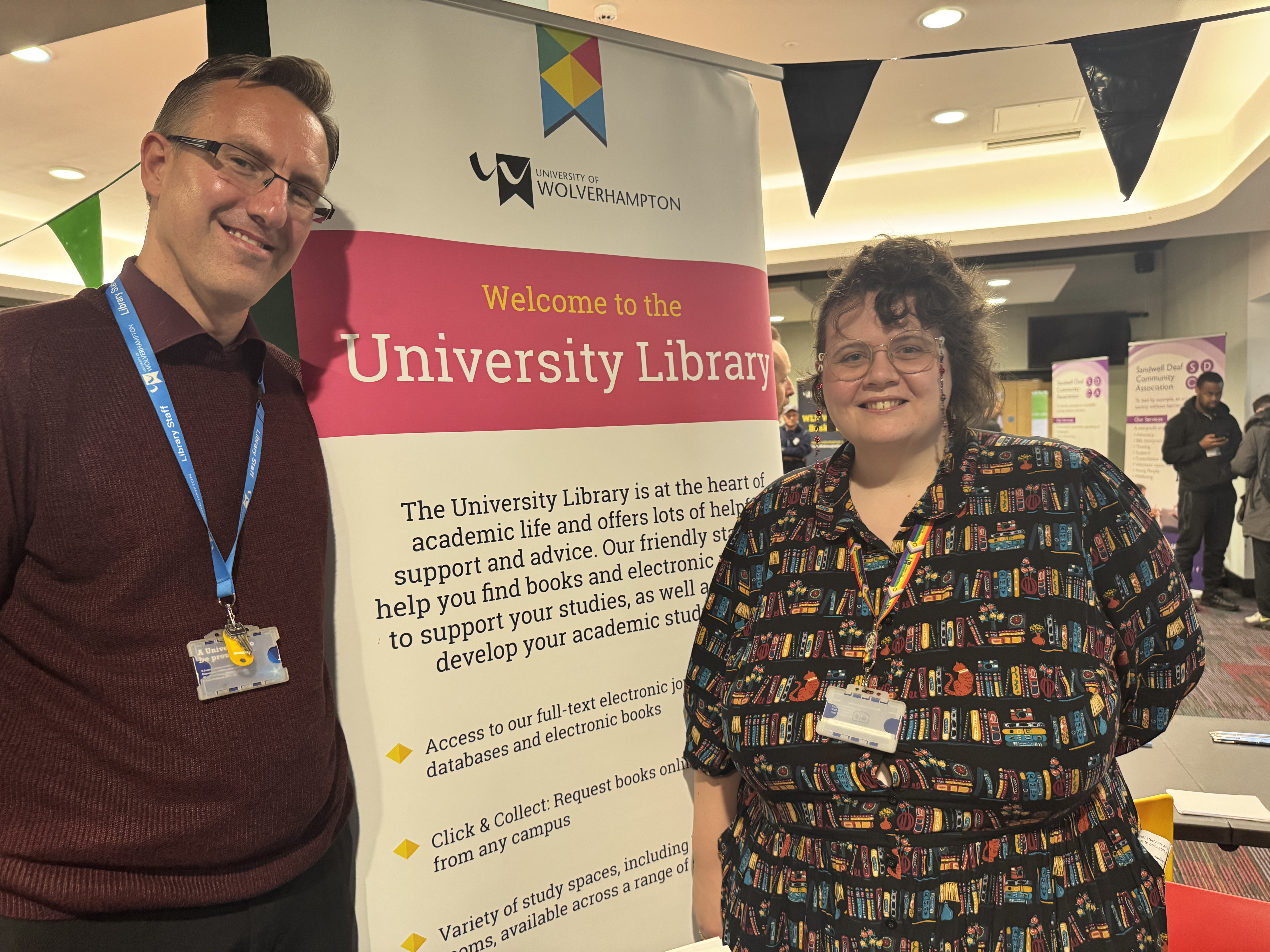 two librarians in front of a sign about the library