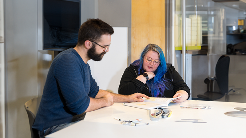 Student sat alongside a librarian looking at some work on a desk