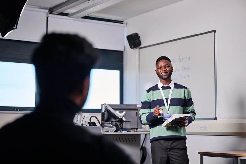 Lecturer holding book talking to students in classroom.