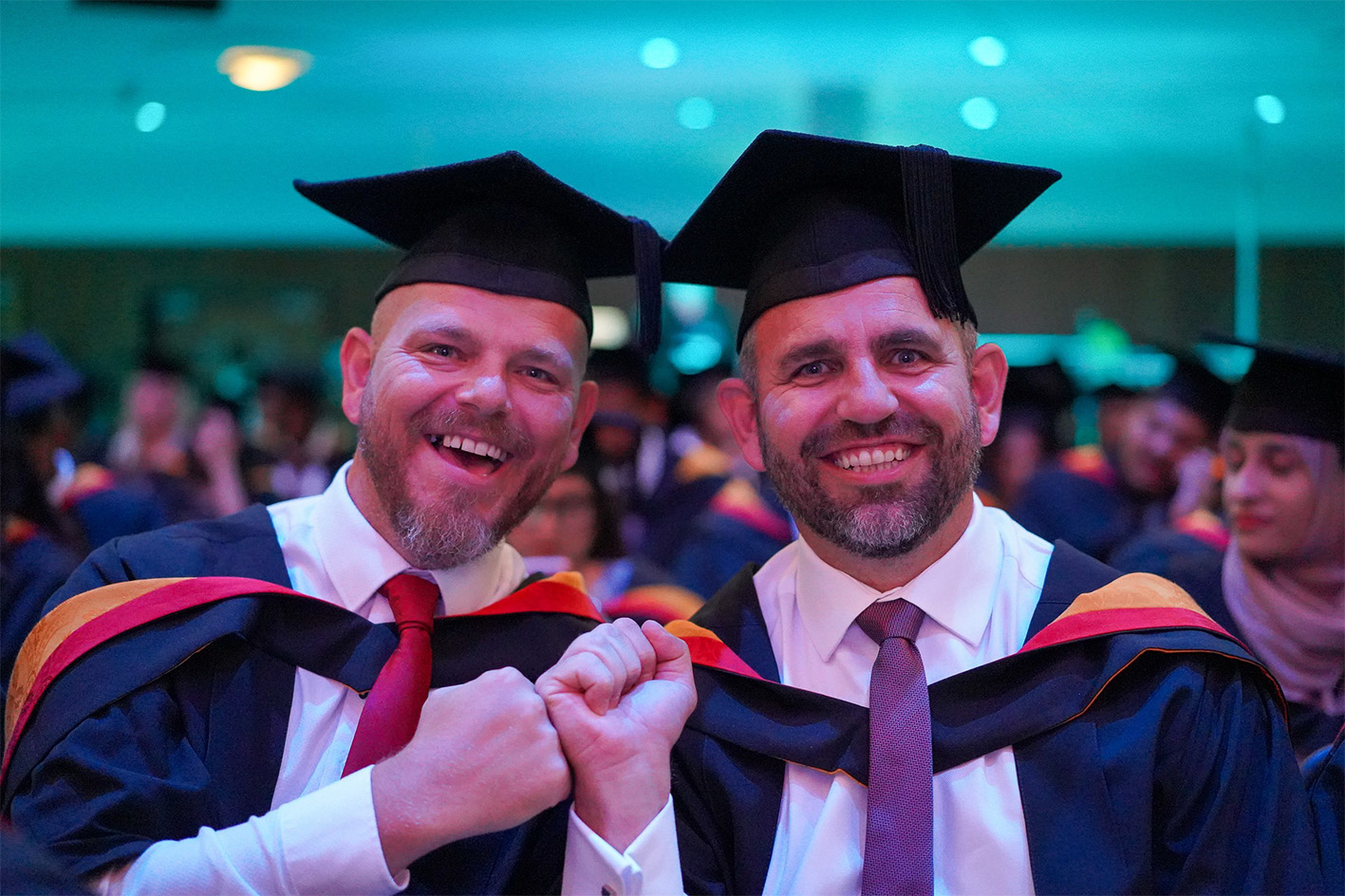 two smiling male graduates fist bump whilst looking at camera