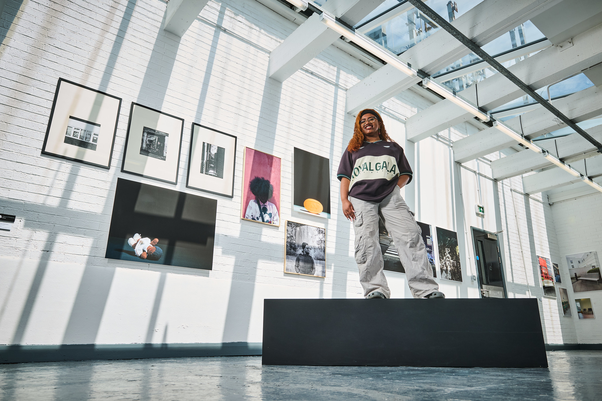 An art student standing in front of a set of framed pieces of art.