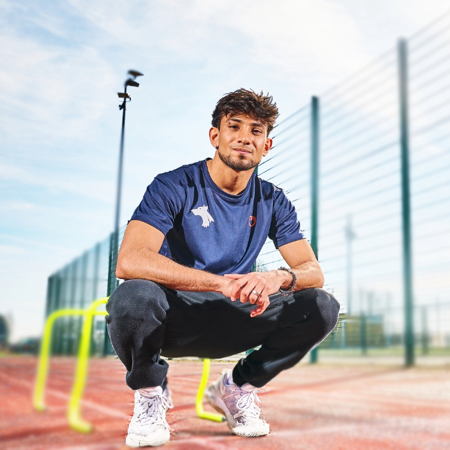 A student in University sports clothing, poised at the start of a running track on Walsall campus.