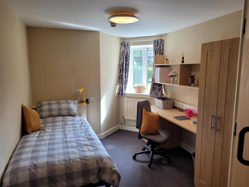 A bedroom in Walsall Campus accommodation, with a bed across from a window, a desk with an office chair and a cupboard