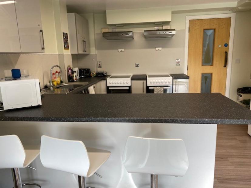 Kitchen in Walsall Campus accommodation with bar stools pulled up to a table, attached to a larger countertop with ovens and cupboards