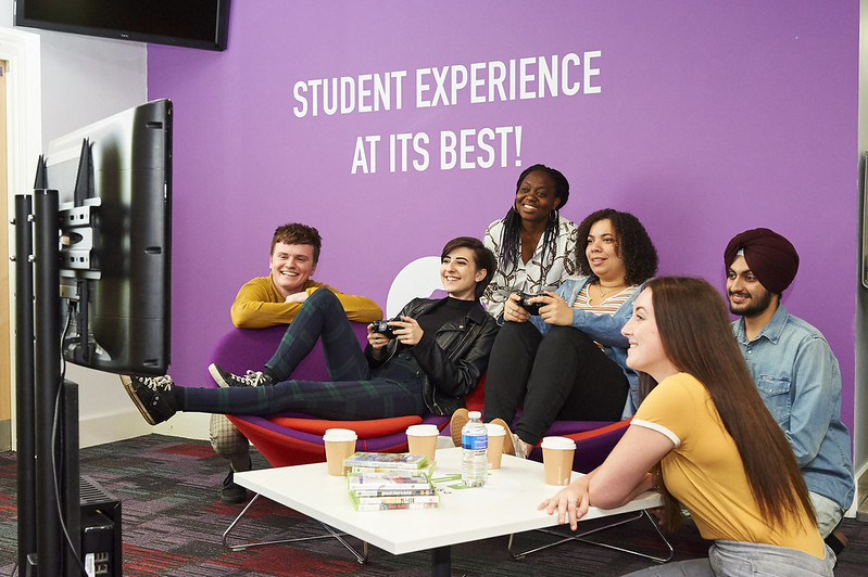 A group of students sitting together, one holding a gaming controller while the others watch