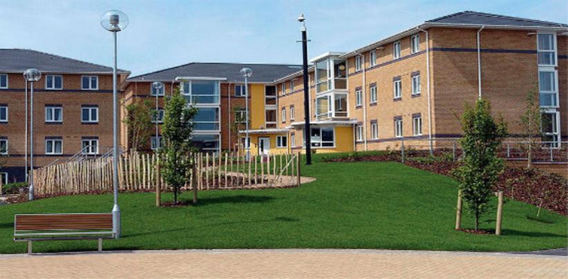 Exterior of Walsall Campus accommodation, green areas with fencing and benches bordering a large building