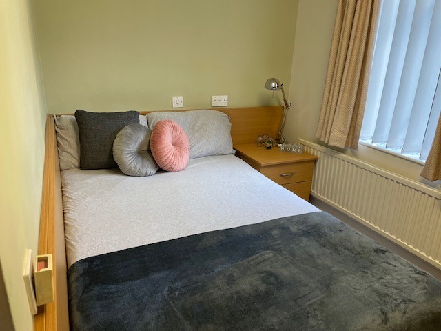 A bedroom in Telford Campus ensuite accommodation, with a bedside table next to a bed overlooked by a window