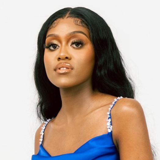 Amanda Nkomo sitting in a white studio, wearing a blue outfit.