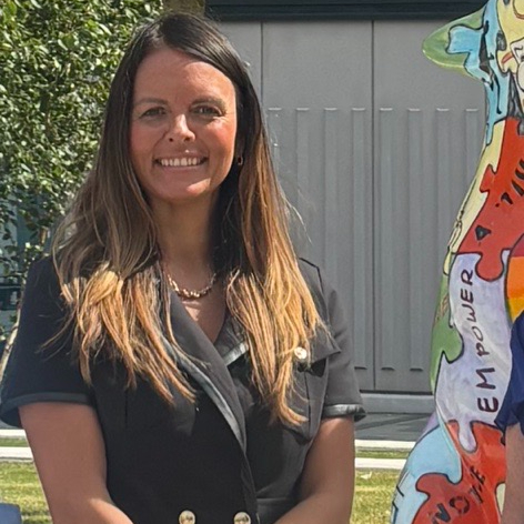 Photograph of Clare Dickens standing by the wolf statue in the City Campus courtyard.