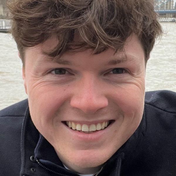 Jack England, wearing a black jacket, photographed next to a body of water.