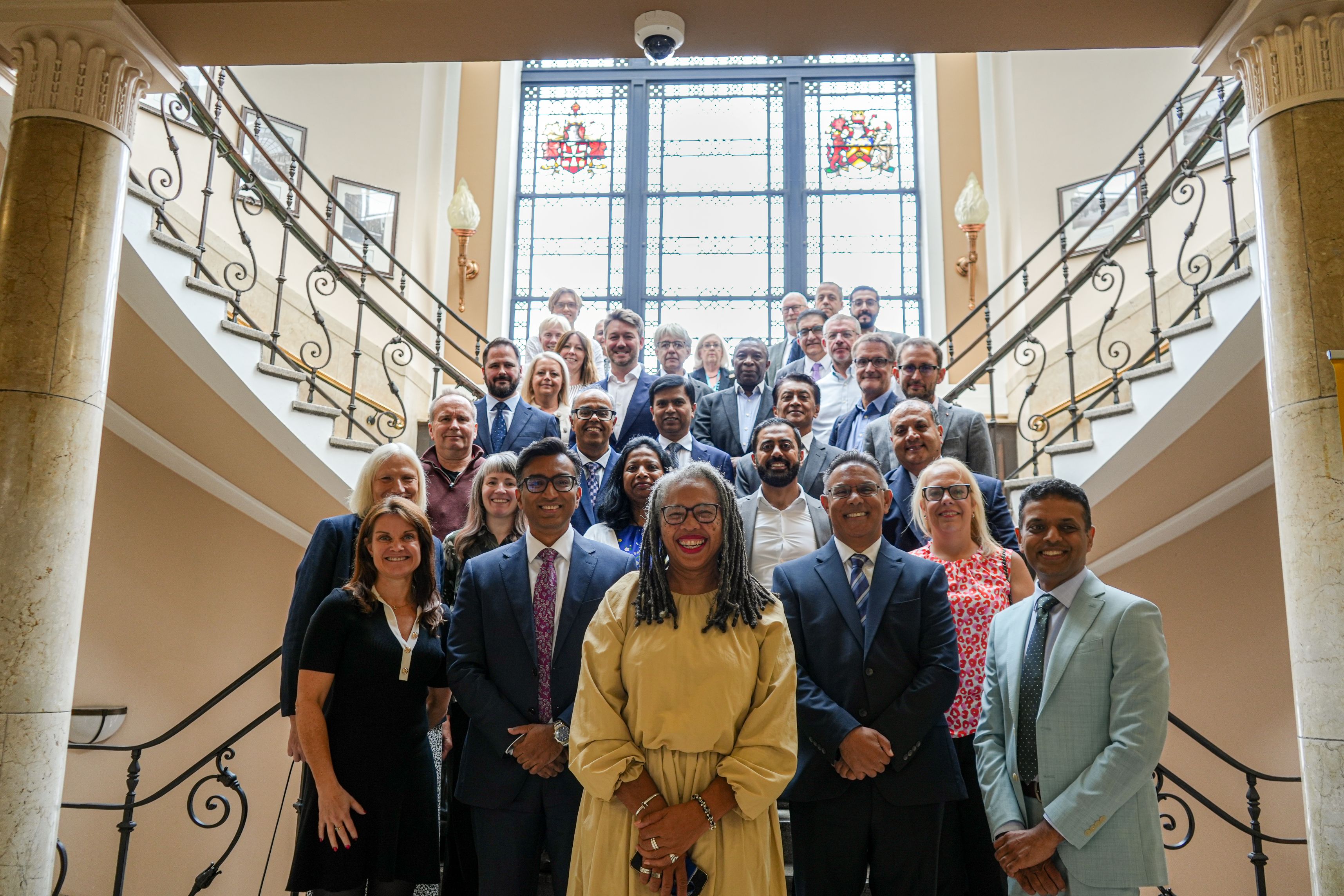 Delegates from the launch event of the clinical trials unit stand in tiers on the steps from reception to the first floor at Wulfruna Building at University of Wolverhampton