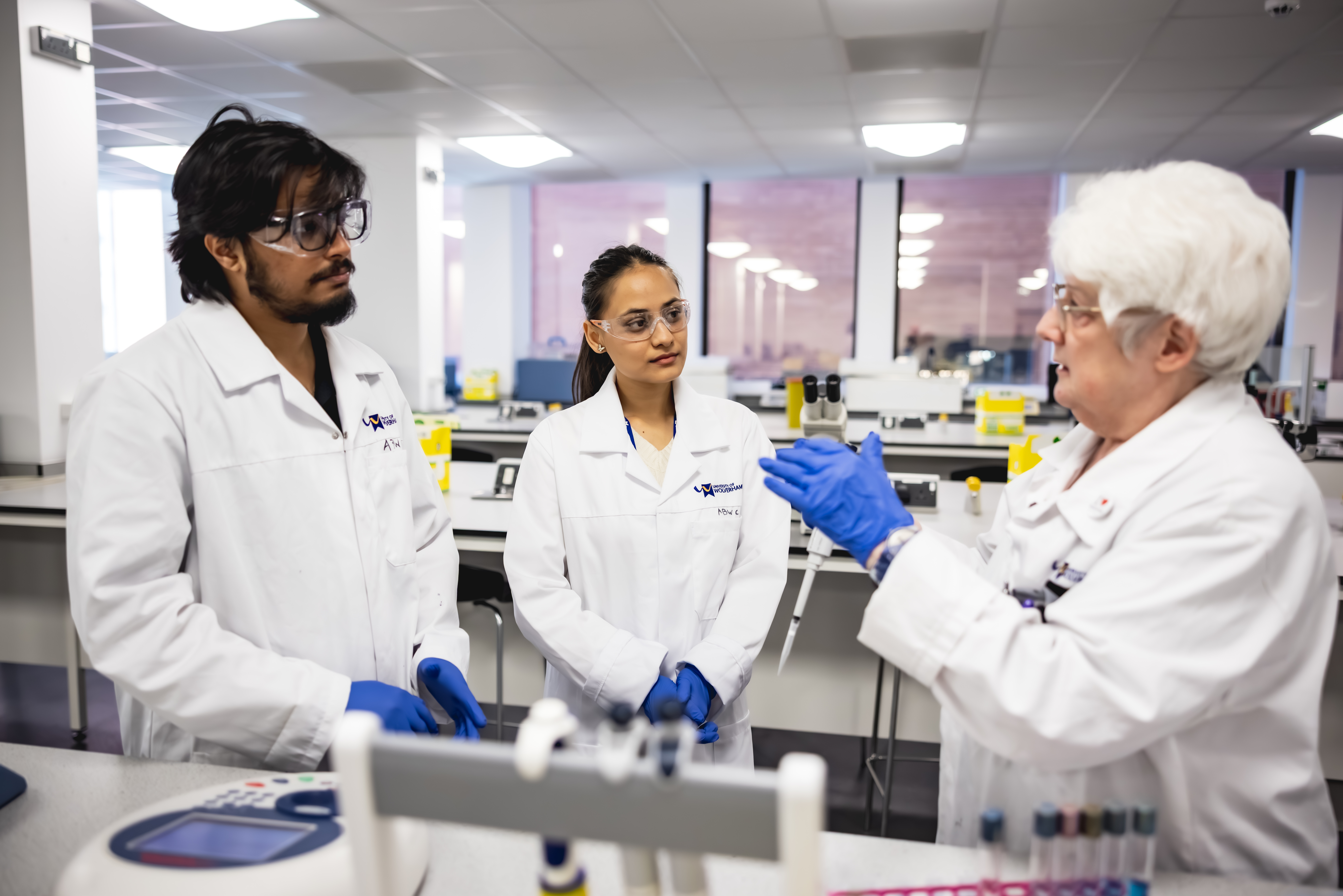 Two students and a lecturer don white lab coats in a laboratory at the University. They are looking at the contents of a test tube.