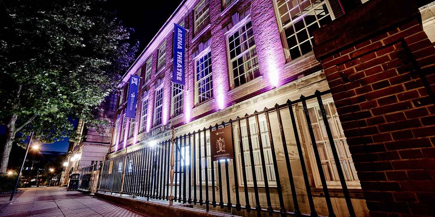 Exterior of the Arena Theatre lit up with purple lights in the night
