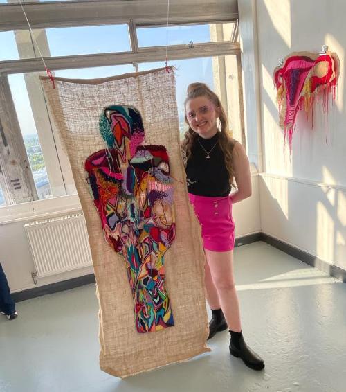 Student posing in front of her work at the annual Degree Show