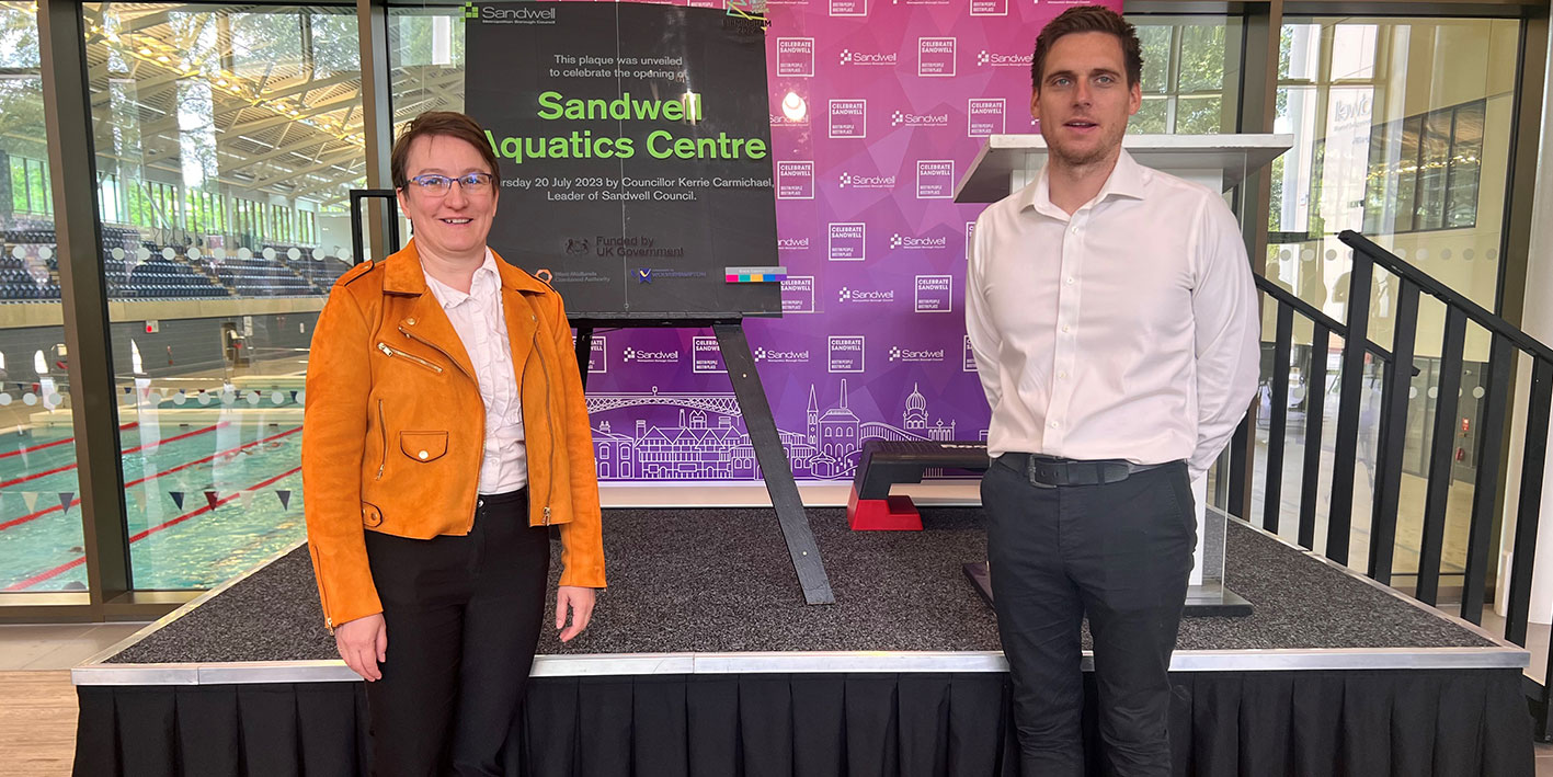 Two members of School of Sport staff standing next to the unveiled plaque for the new Sandwell Aquatics Centre