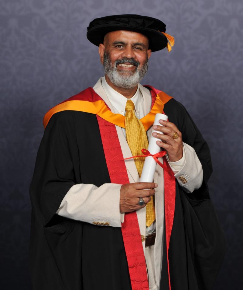 Honorary Graduate Peter Chand holding his award and smiling at the camera