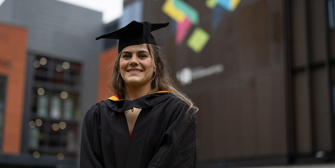 A portrait of a female graduate smiling in the University courtyard