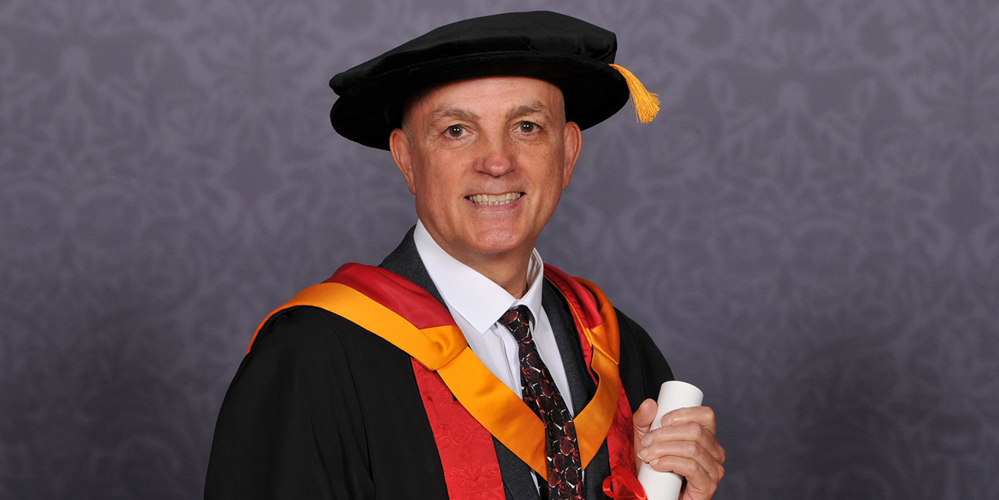 A portrait of Honorary Graduate Shaun Aldis holding his award