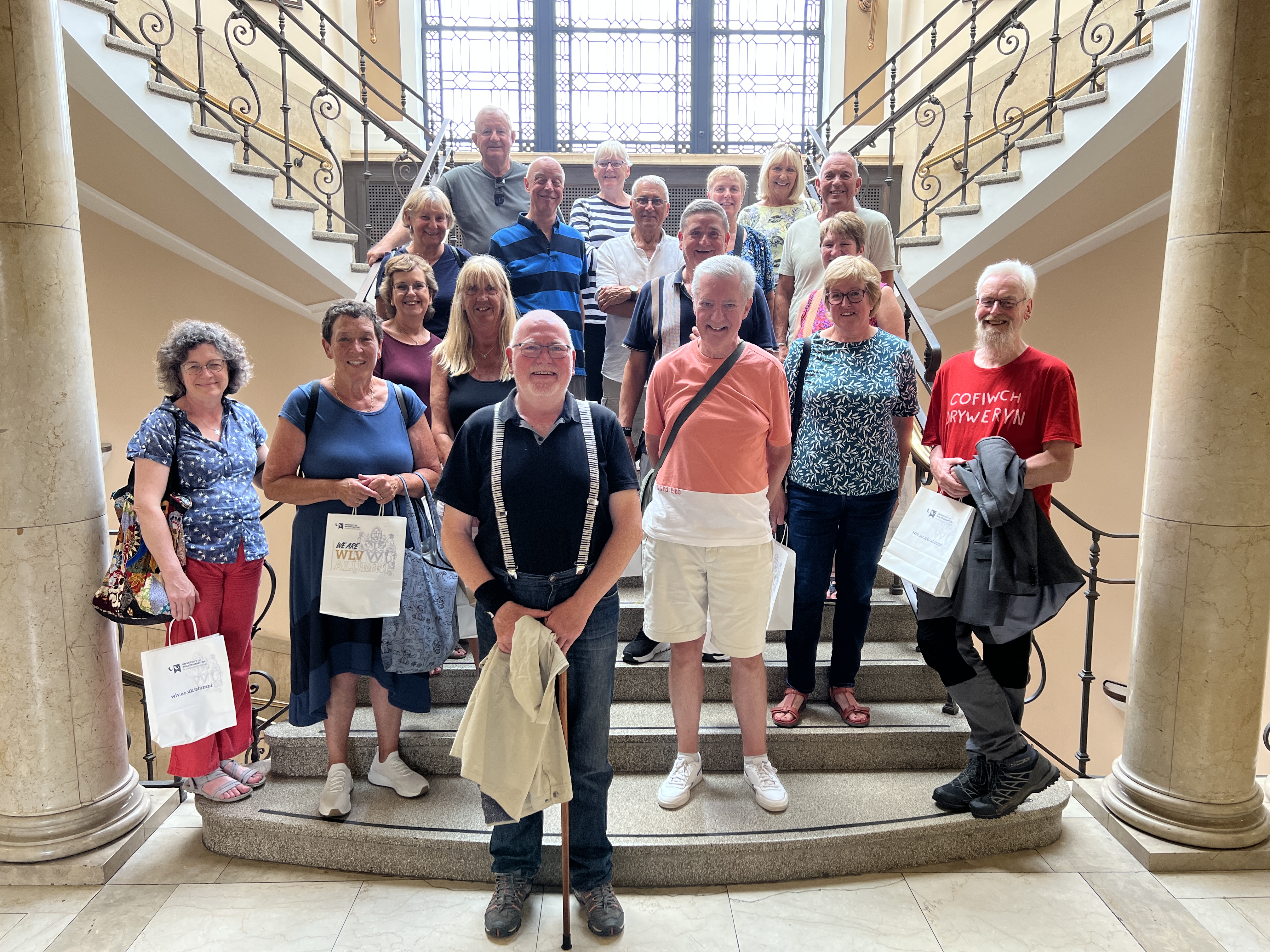 A group of alumni visit the university after 50 years standing on the main stairs