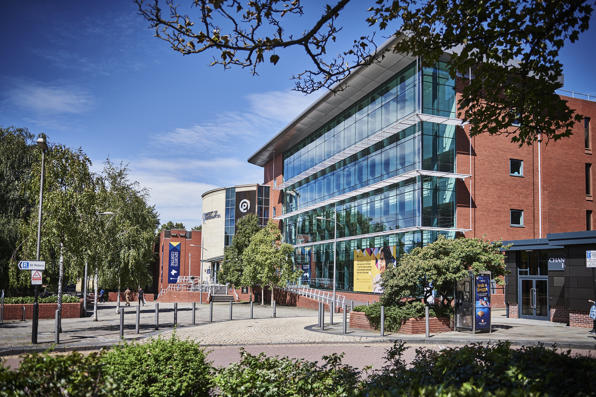 Exterior of the Ambika Paul building on a sunny day, a red-brick building with a large wall of windows currently decorated with a large graphic of a student.