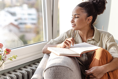 woman looking out window while journaling