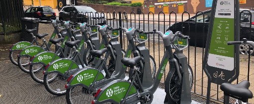 A line of electric bikes at a docking station looking out onto a road
