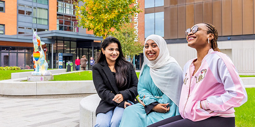 three global majority students sitting in City courtyard