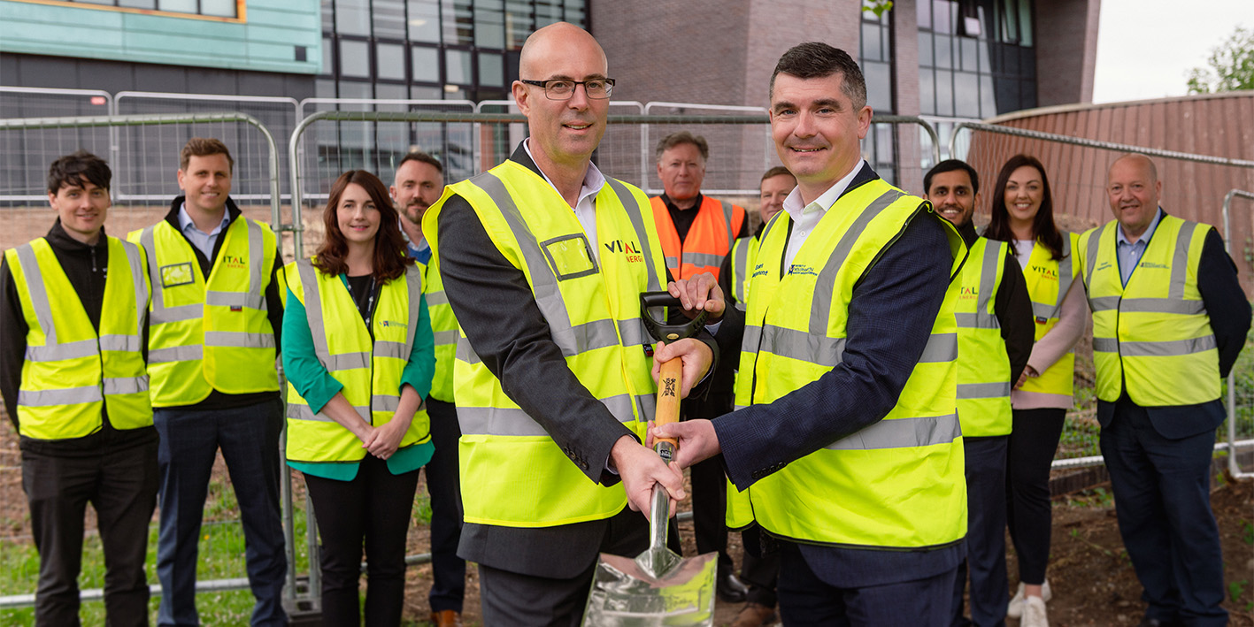 Phil Mottershead and Pete Cross hold up a spade with project team in background at decarbonisation ground breaking event at Walsall Campus