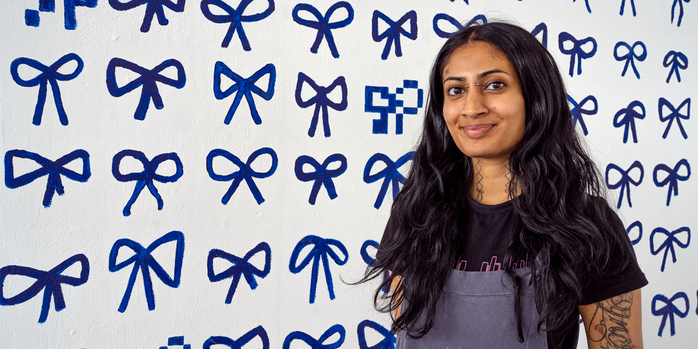 Simmi Sahota Fine Art student in front of degree show piece - a wall mural covered in painted blue bows