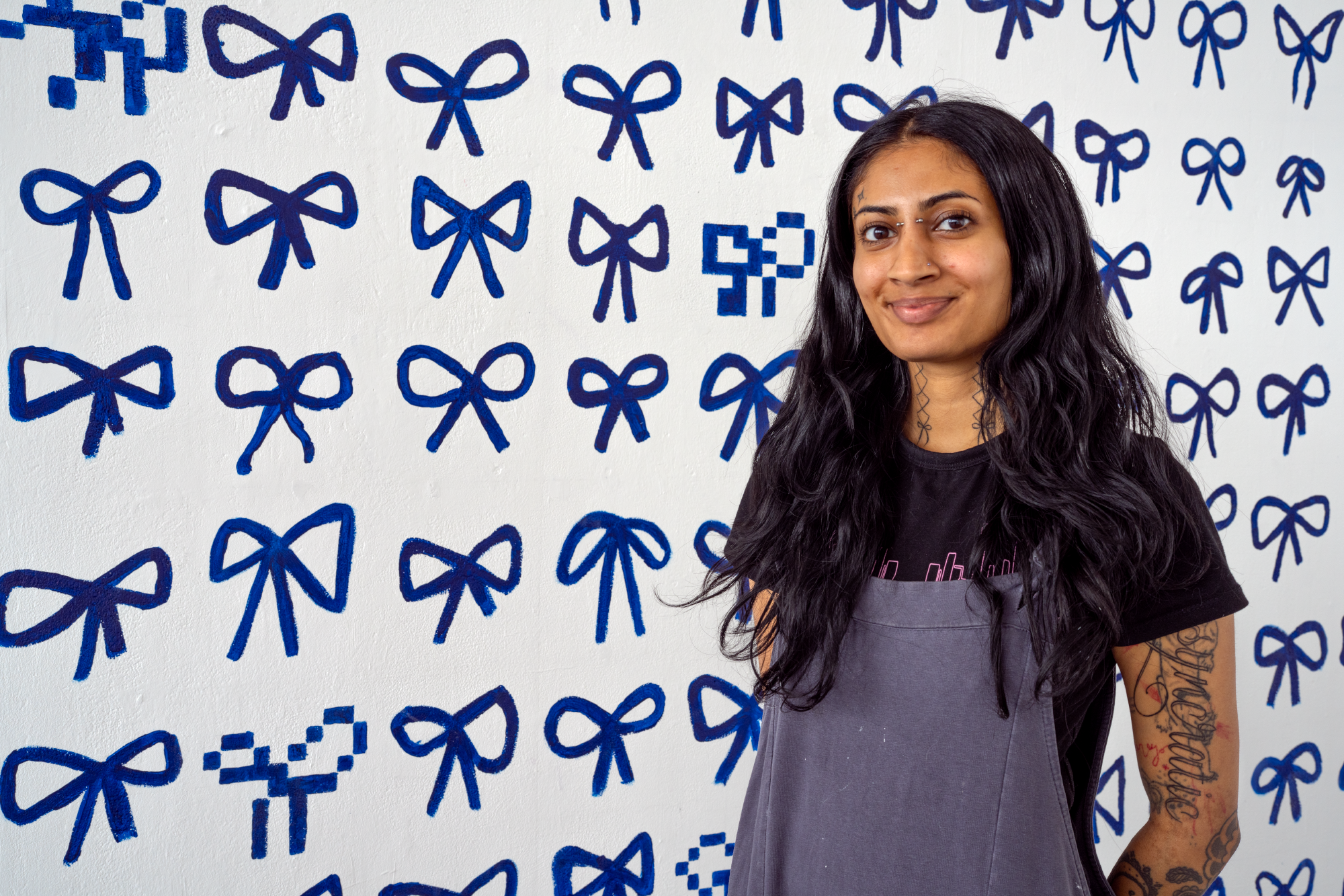 Simmi Sahota Fine Art student in front of degree show piece - a wall mural covered in painted blue bows