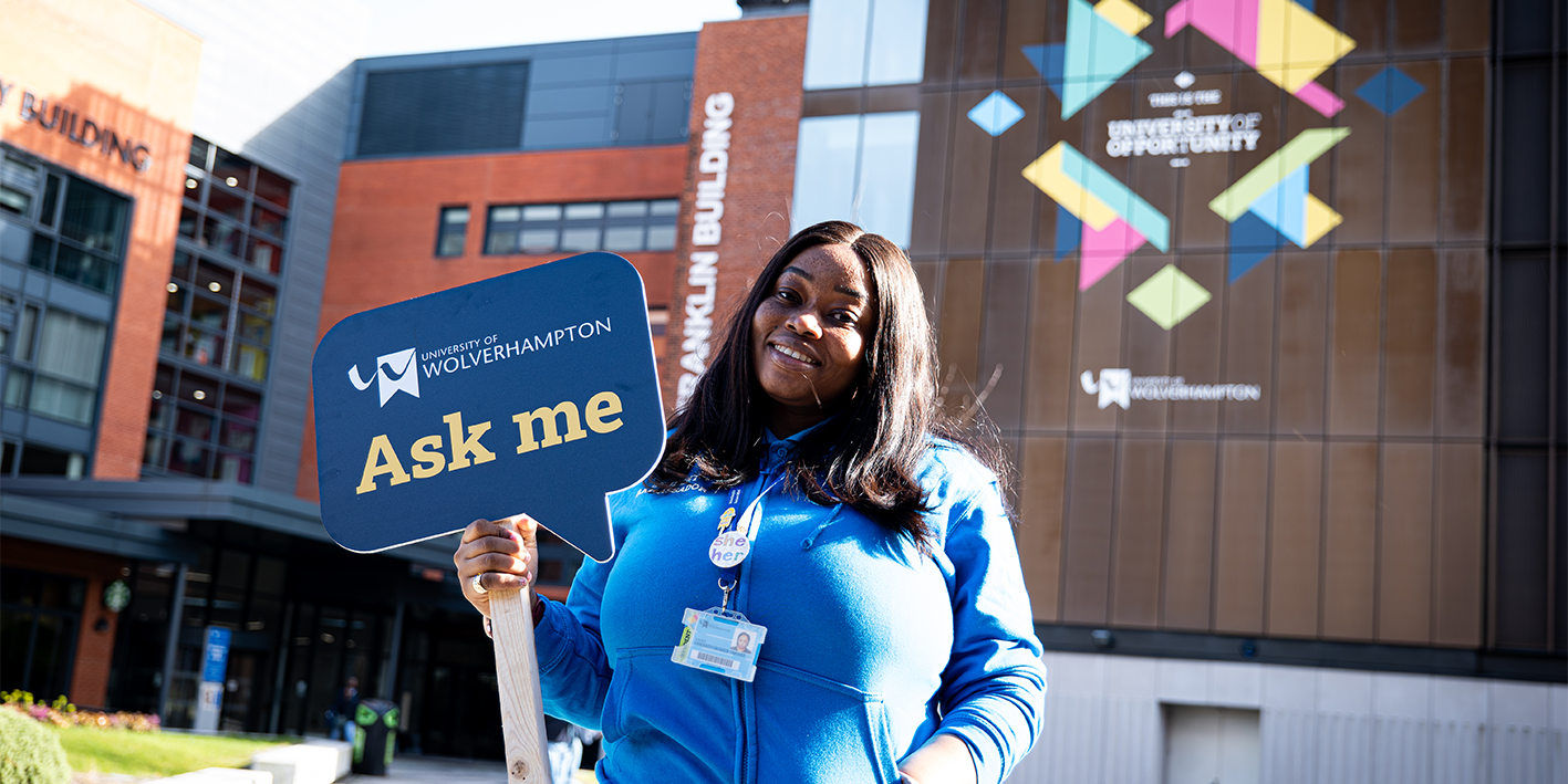 smiling Student Ambassador holding Ask me sign in the Courtyard