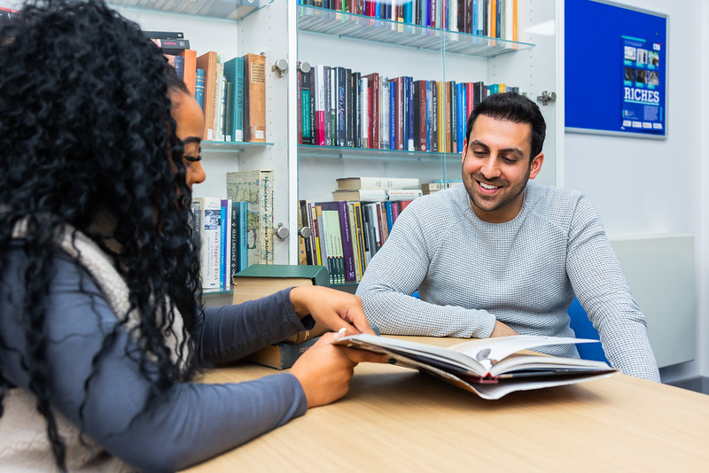 two students looking at text book in the library