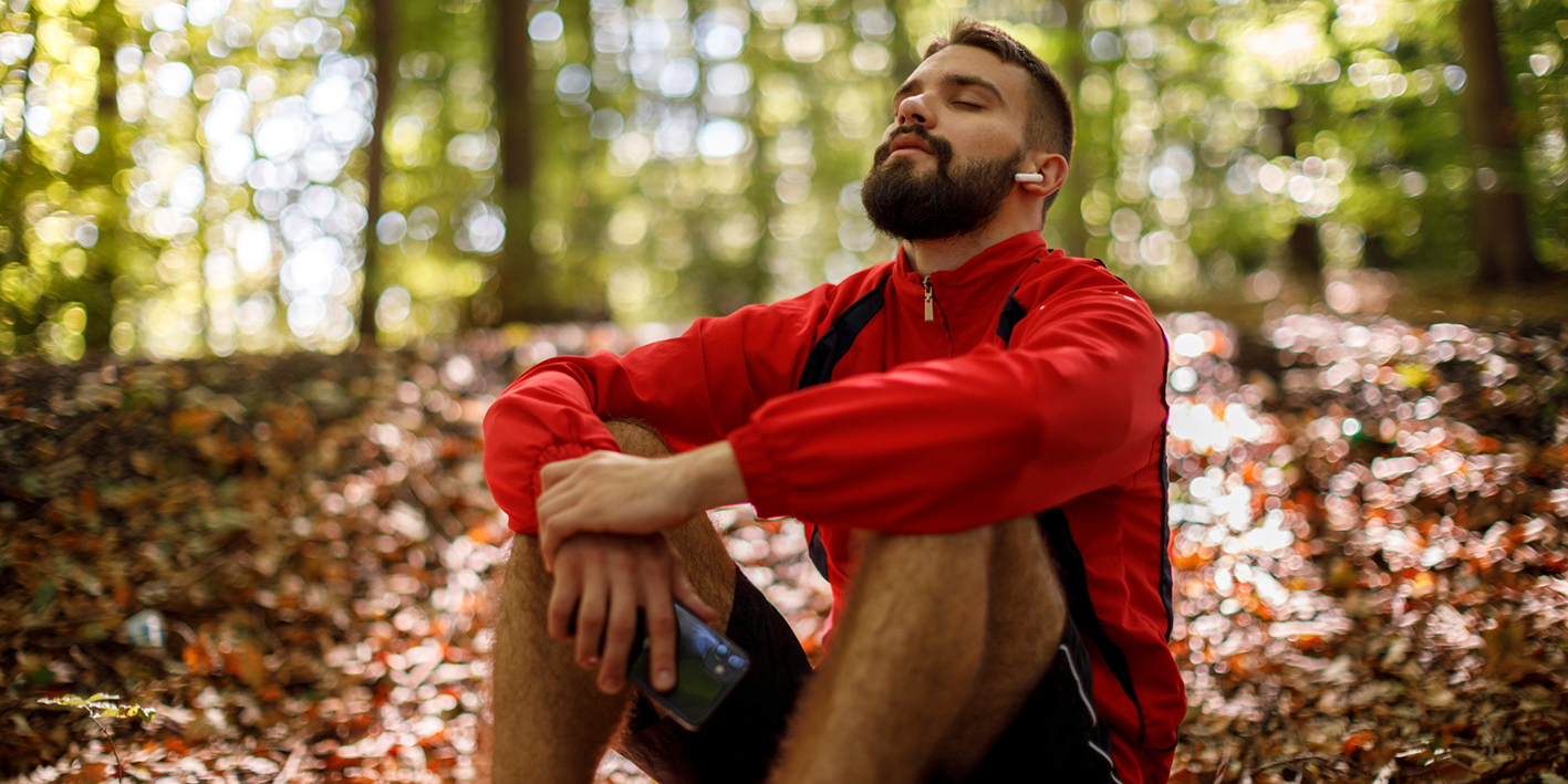 man in sports clothing sitting in a forest listening to something on his phone