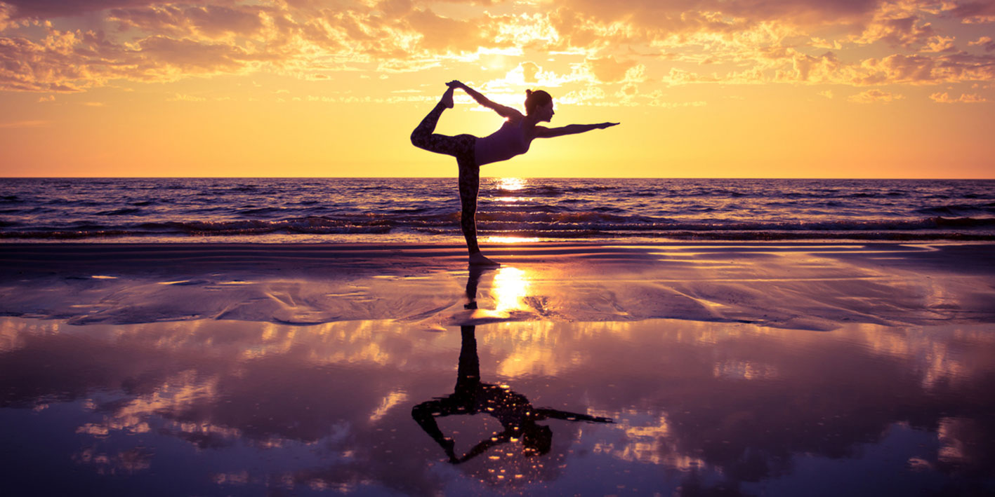 An image depicting a woman in a yoga pose on the beach in the sunset