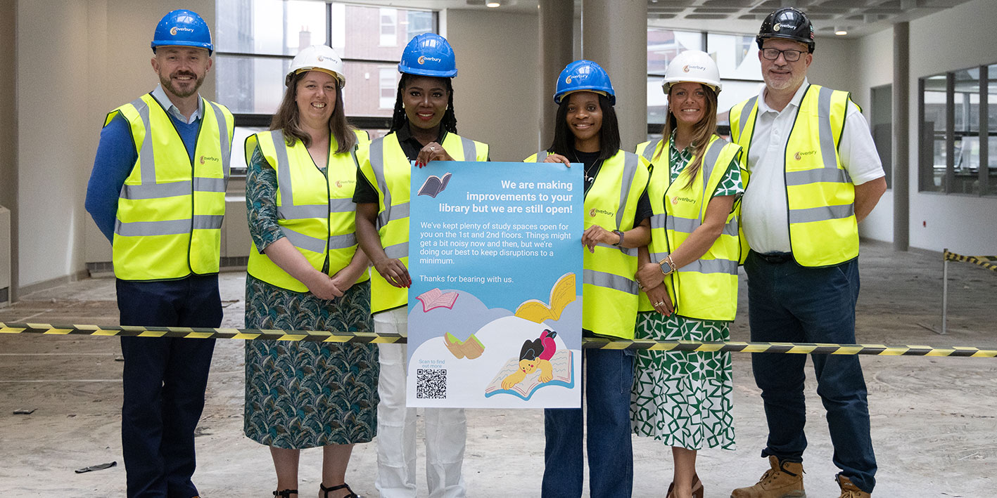 A group of people in hard hats and hi viz standing in front of a library room which is being refurbished