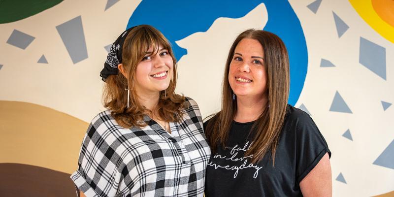 A portrait of two graduates with the mural they designed