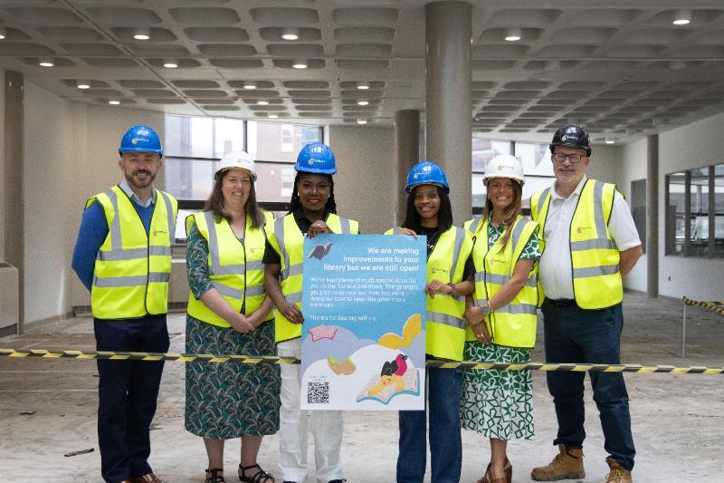 A group of people in hard hats and hi viz standing in front of a library room which is being refurbished