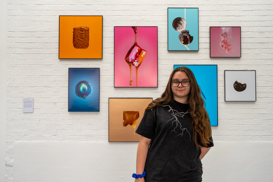 Photography student Millie Elizabeth Elkington stands in front of her exhibition - a series of brightly coloured food photography pieces
