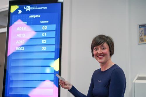 smiling student standing next to the ASK queuing system holding a ticket