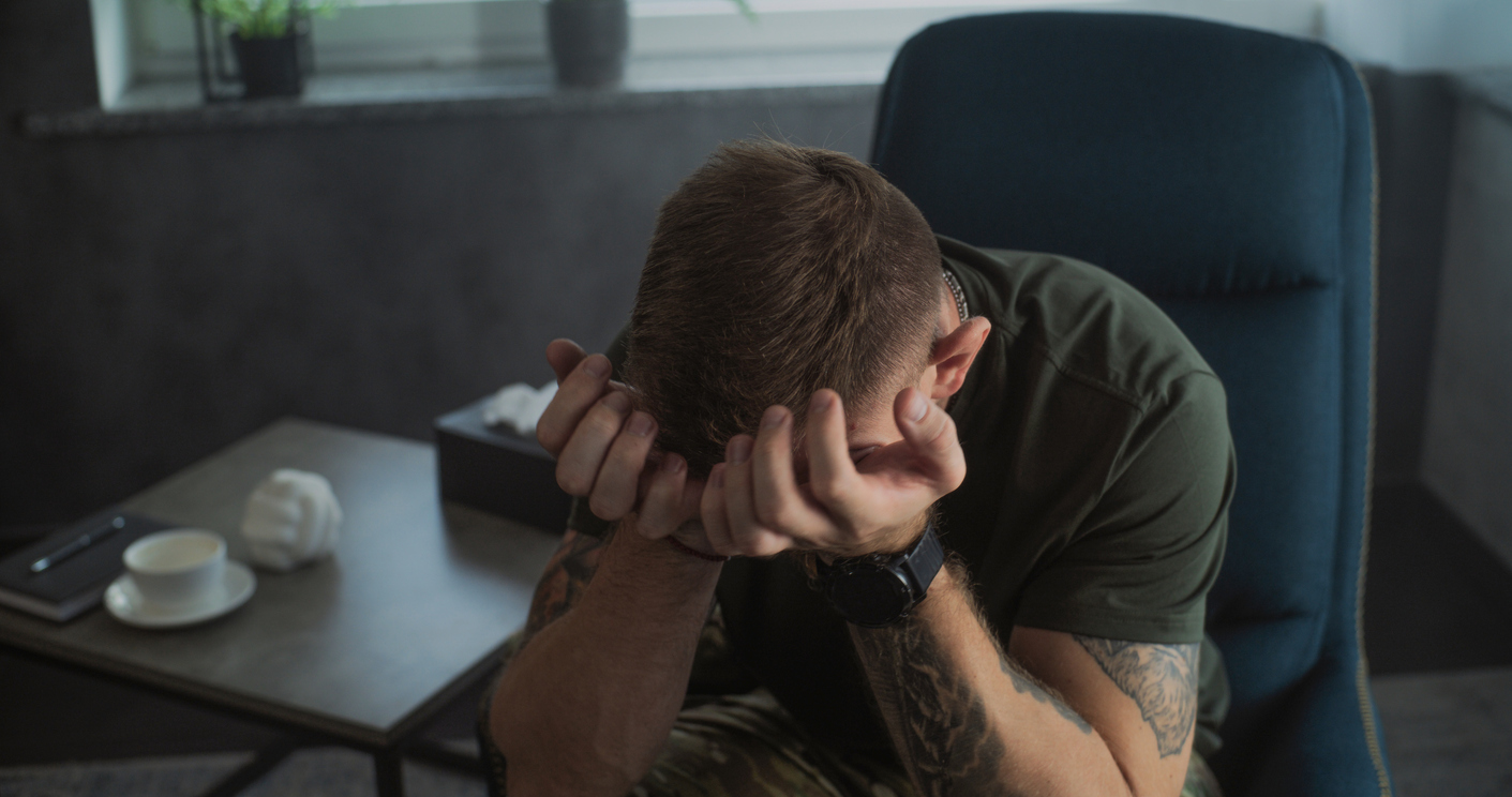 a man in a dimly lit room suffering from distress, holding his head in hands