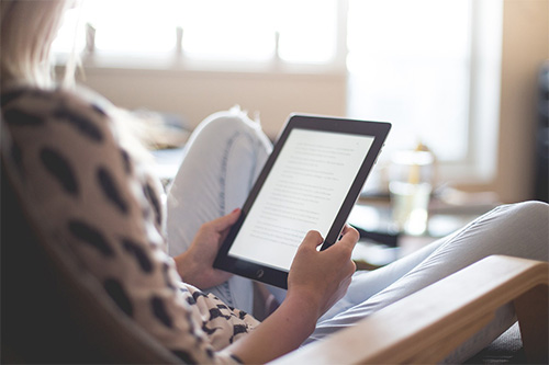 woman, sitting comfortably, using an e-reader or tablet