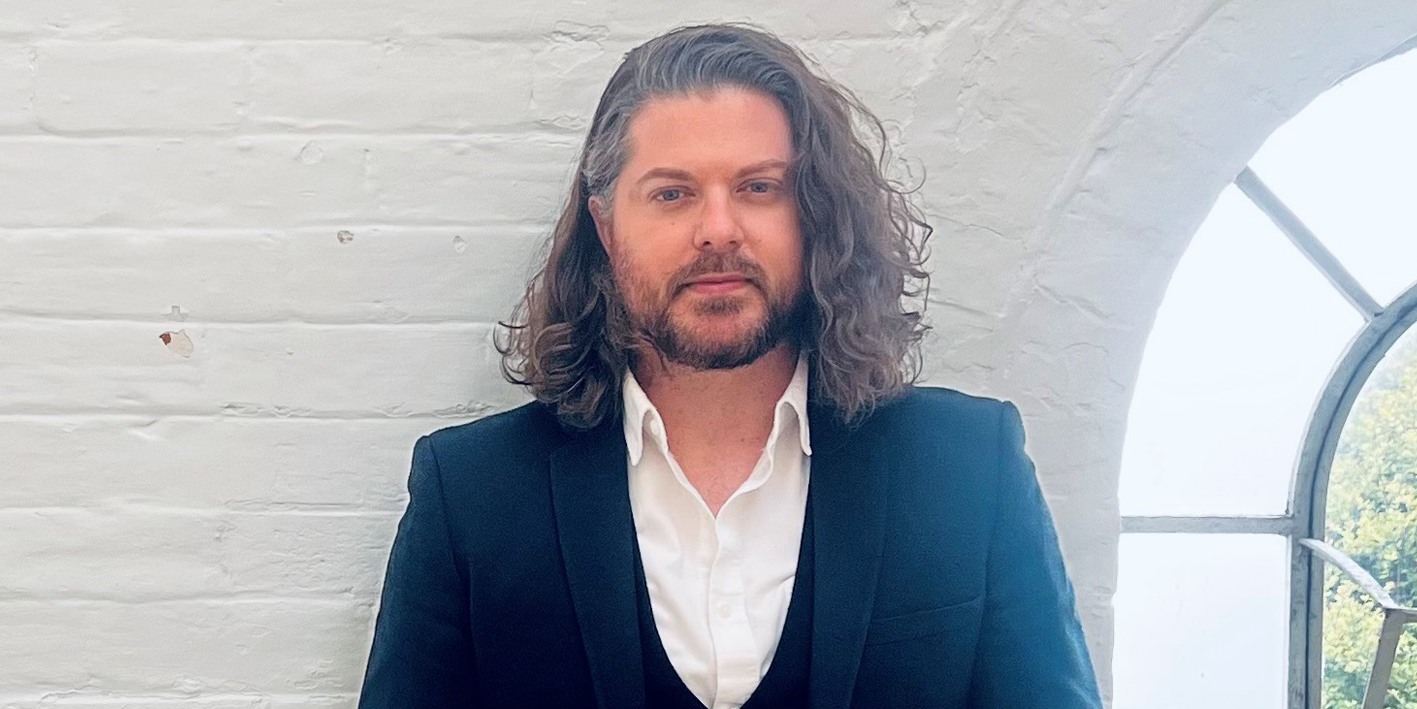 MsC psychology alum Leon Mitchelle in suit standing against a white brick wall